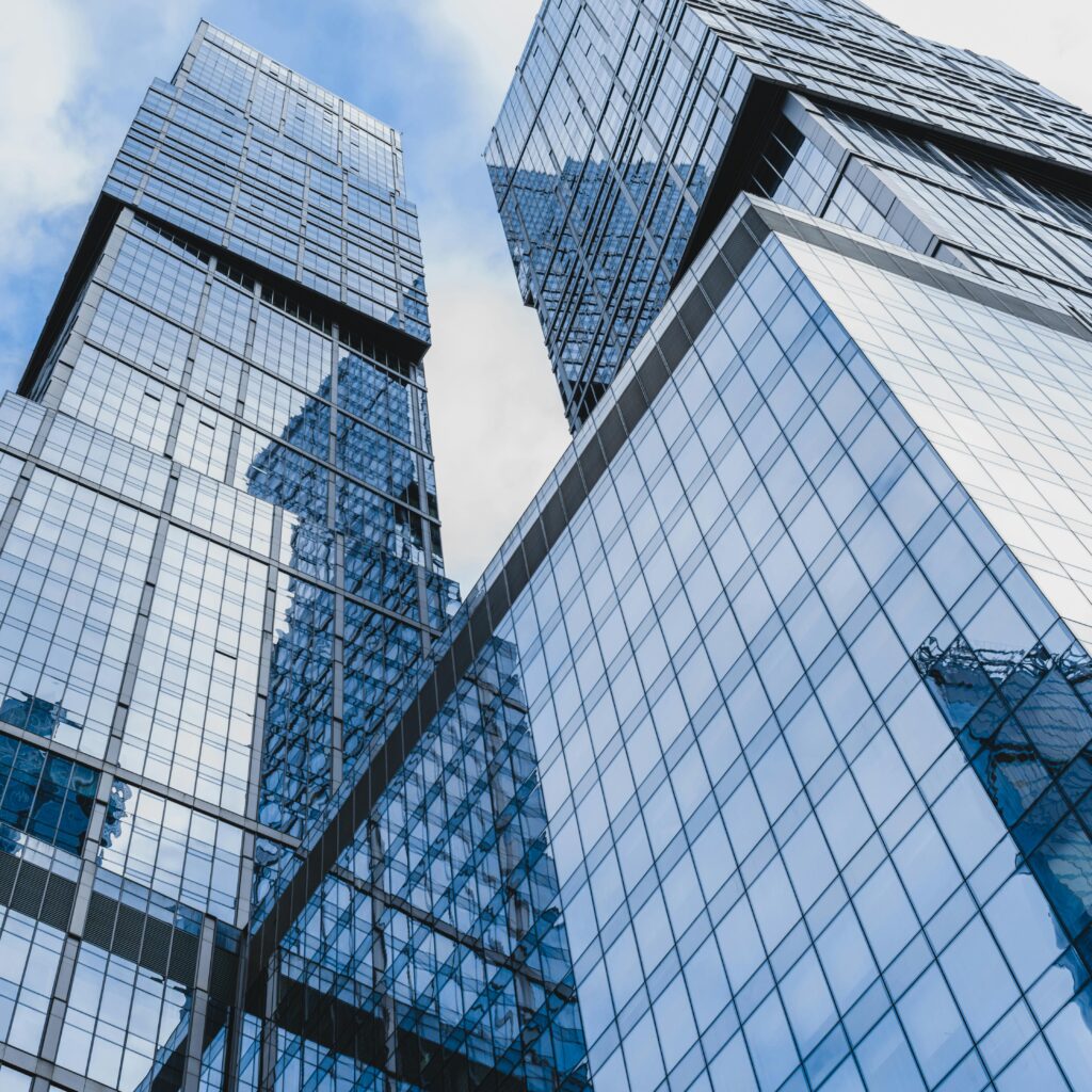 Low angle shot of towering glass skyscrapers reflecting blue skies in a modern cityscape.
